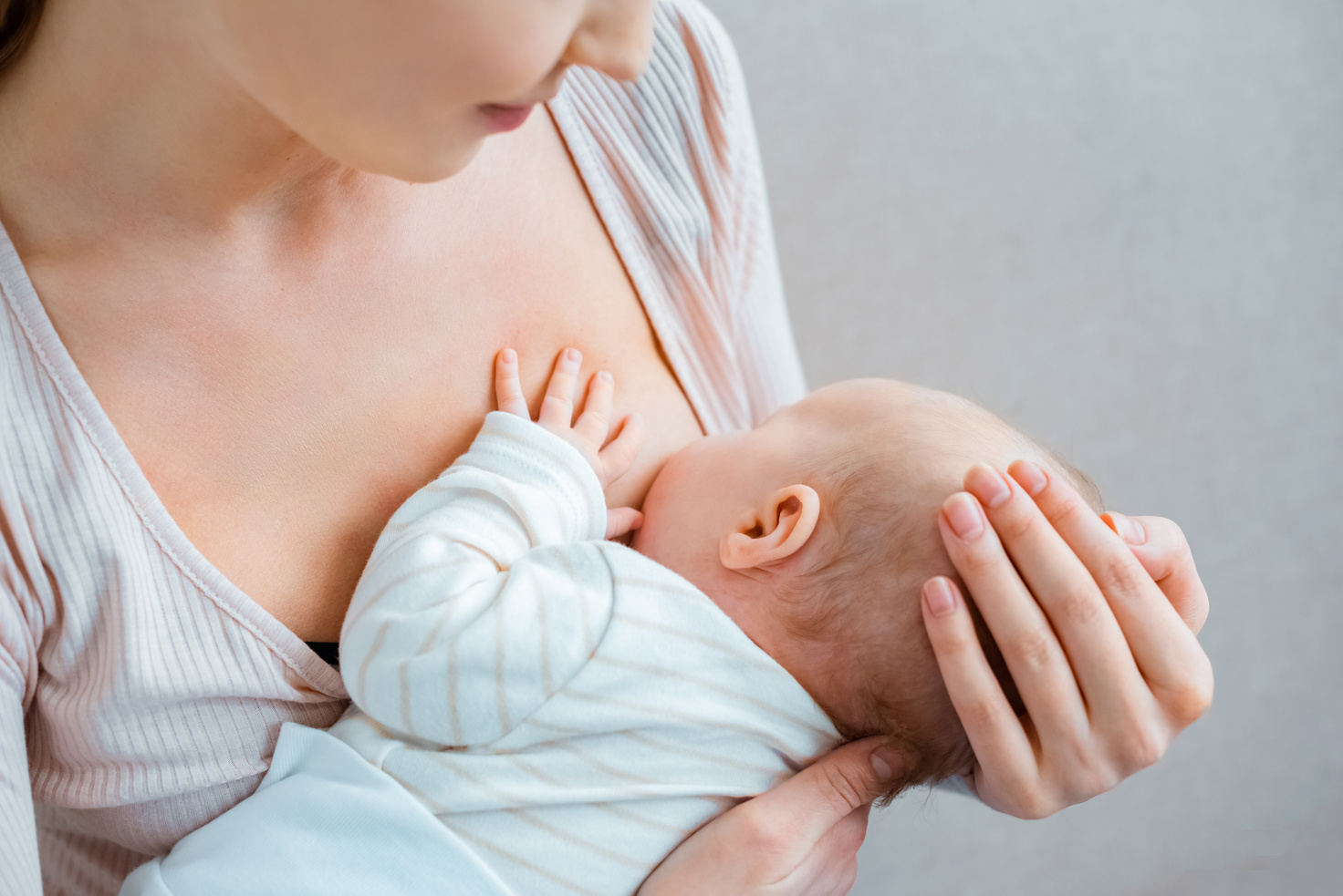 cropped shot of young woman breastfeeding baby on grey